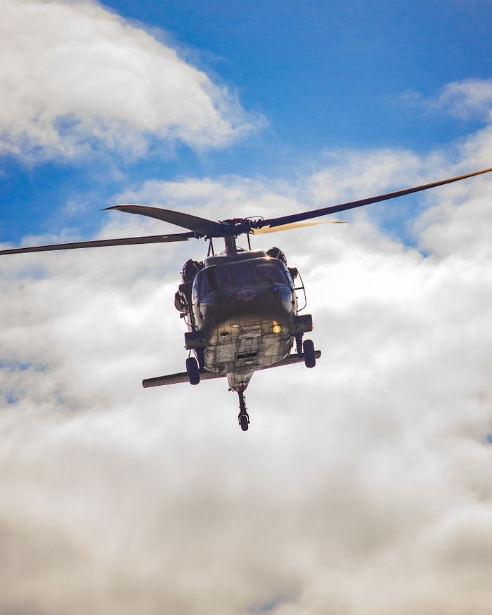 services-02 A helicopter soaring above the clouds in a powerful flight against a clear blue sky.