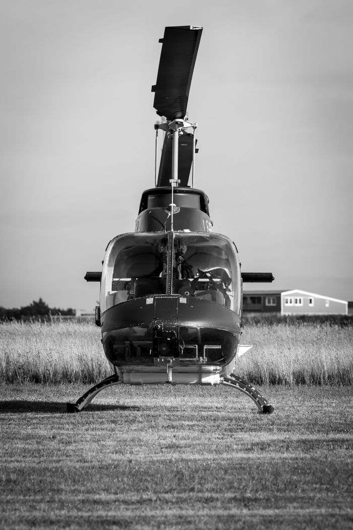 why-choose-us Front view of a helicopter parked on a grass field in black and white.