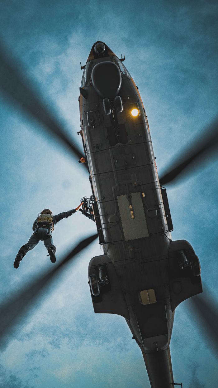 gallery-2 A person performing a daring helicopter rescue in a dramatic sky setting.