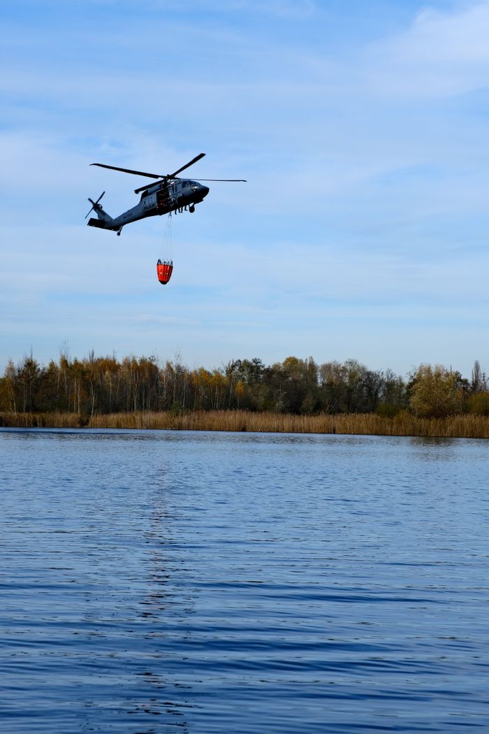 hero-img-02 A helicopter captures water from a lake in scenic Poland's autumn landscape.