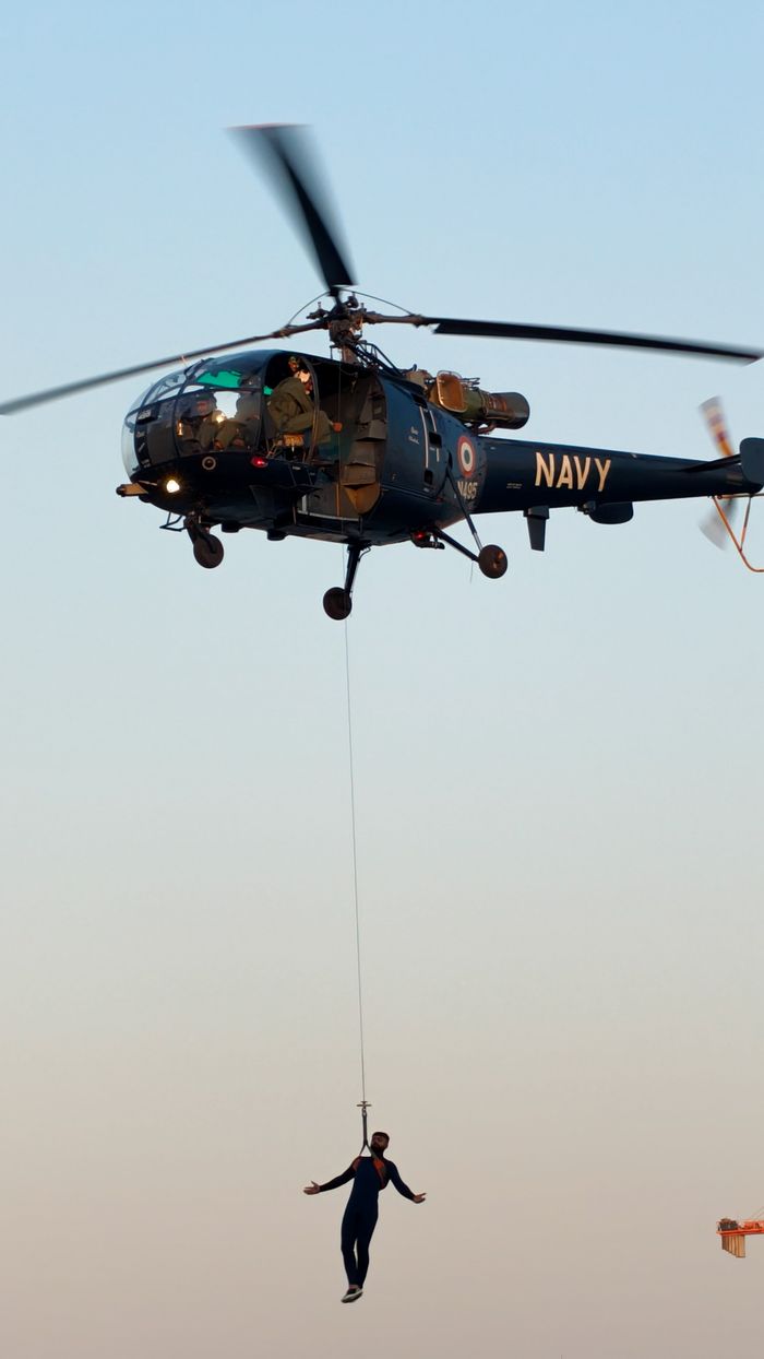 gallery-1 A navy helicopter performing a daring rescue operation with a person suspended below at dawn.